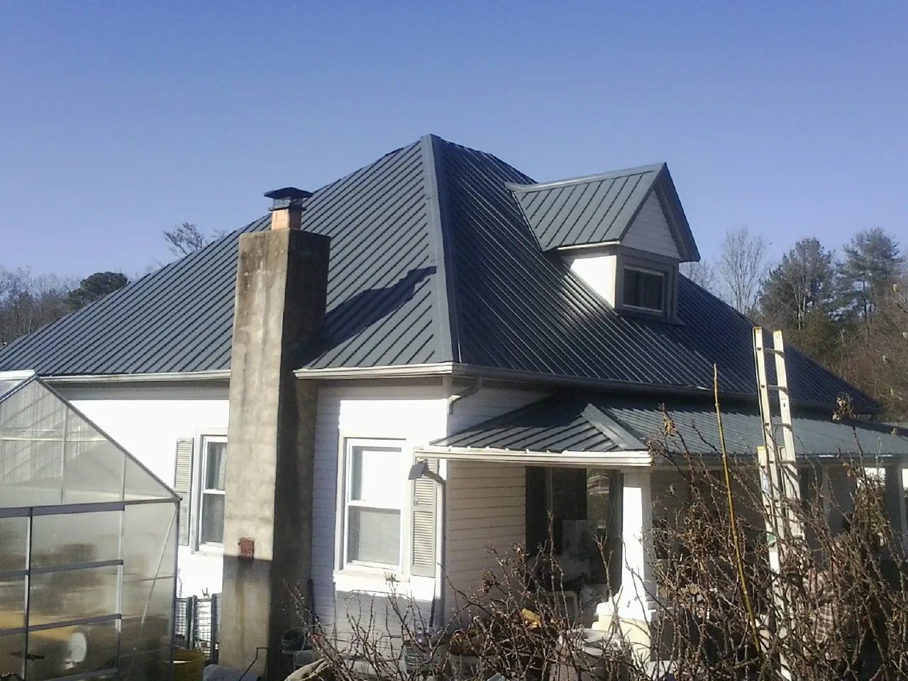 Dark blue standing seam metal roof on a white farmhouse with dormer — Slate & Tile Roof Repair by Roofing Brothers in Bayville