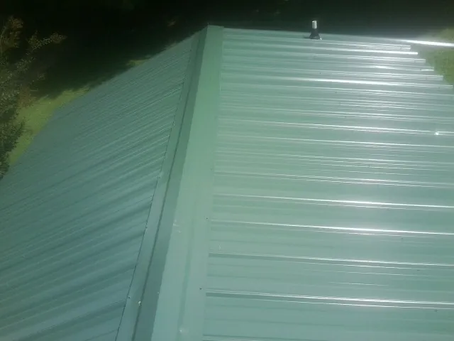 New green metal panels meeting at the ridge of a roof — Flat Roof Repair work by our crew in Bayville
