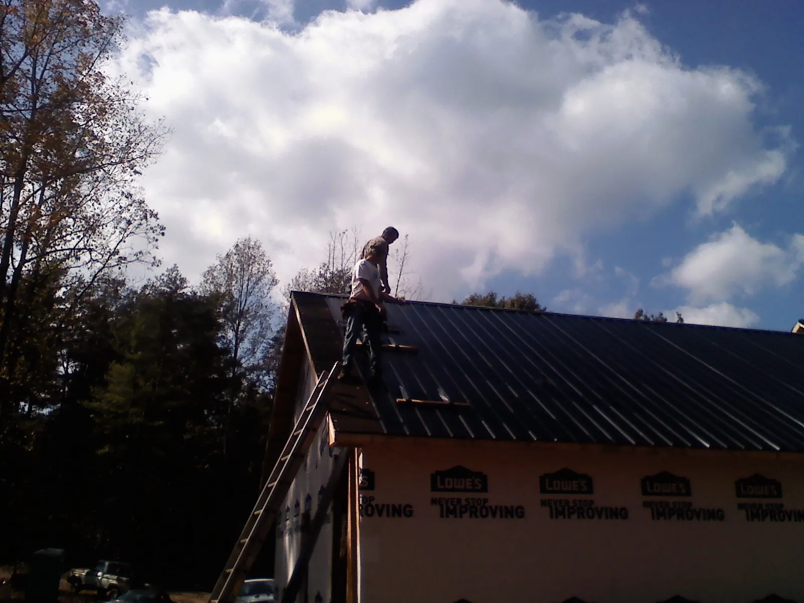 Roofer fastening dark metal panels high against a cloudy sky, from a Roof Inspection job in Bayville