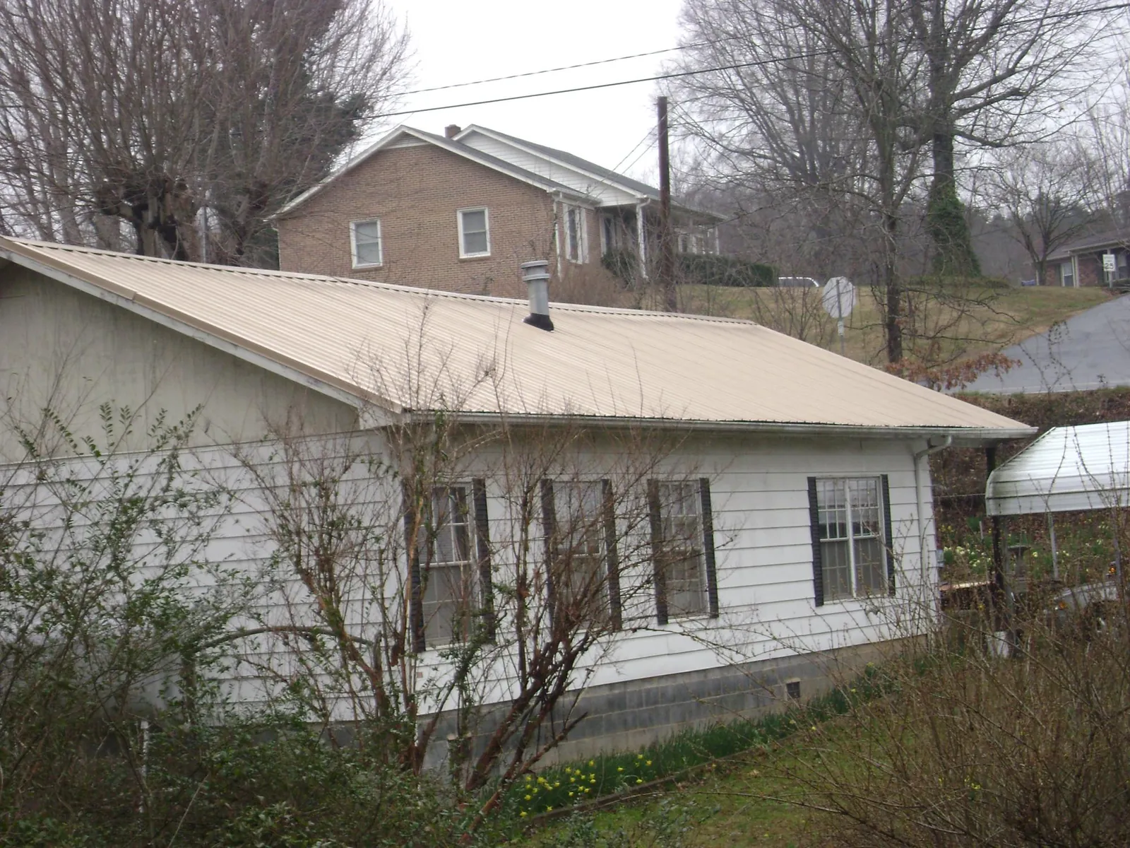 Tan metal roof on a white sided house set into a hillside — Commercial Roofing by Roofing Brothers in Bayville